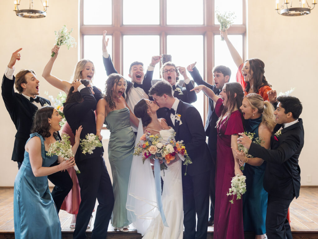 Bride and groom kissing as their wedding party celebrates during an Austin wedding