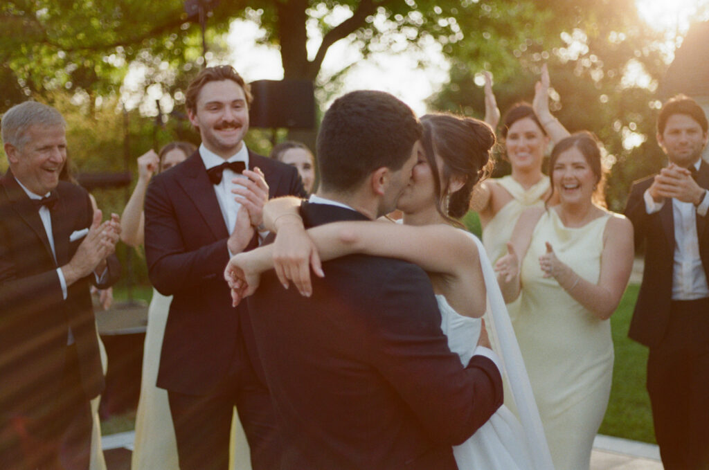 Bride and groom kissing as guests celebrate during an outdoor Austin wedding reception