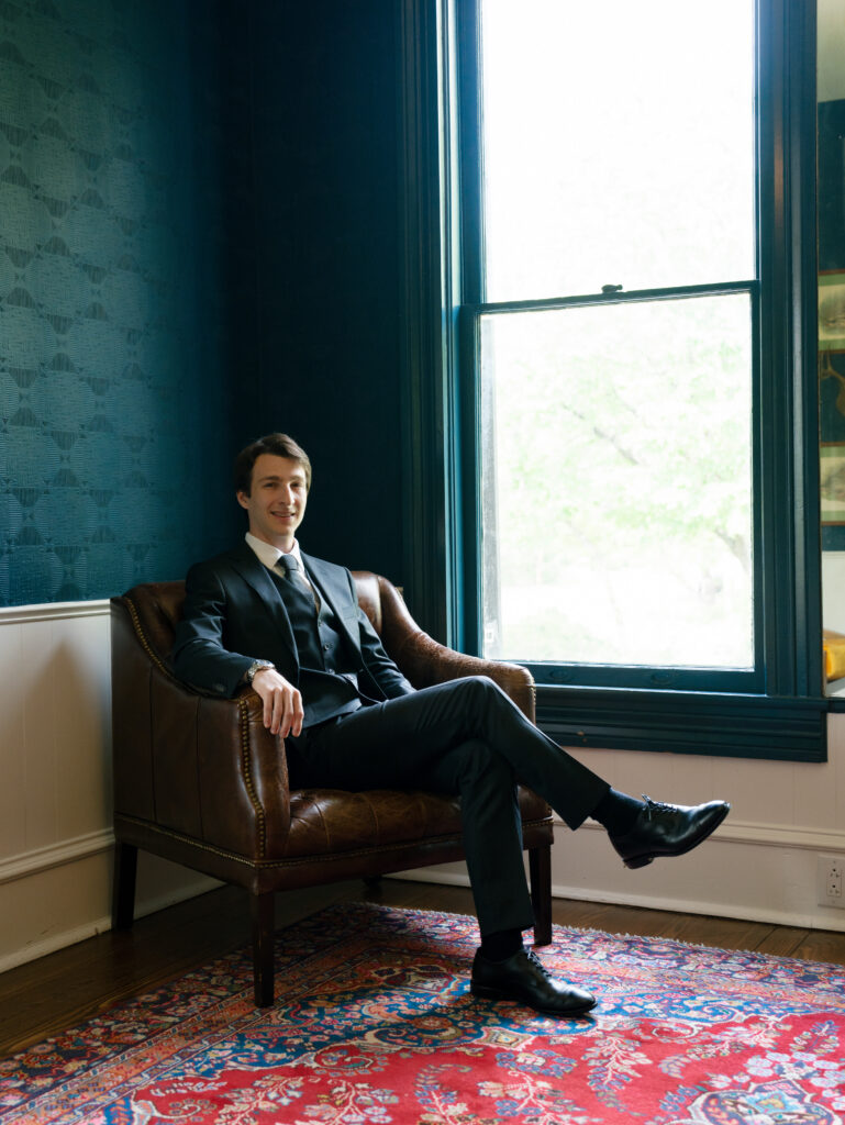 Groom seated by a window inside Woodbine Mansion before the wedding ceremony.