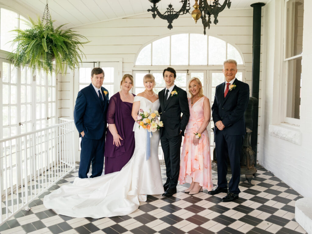 Newlyweds posing with their parents inside the bright sunroom at Woodbine Mansion.