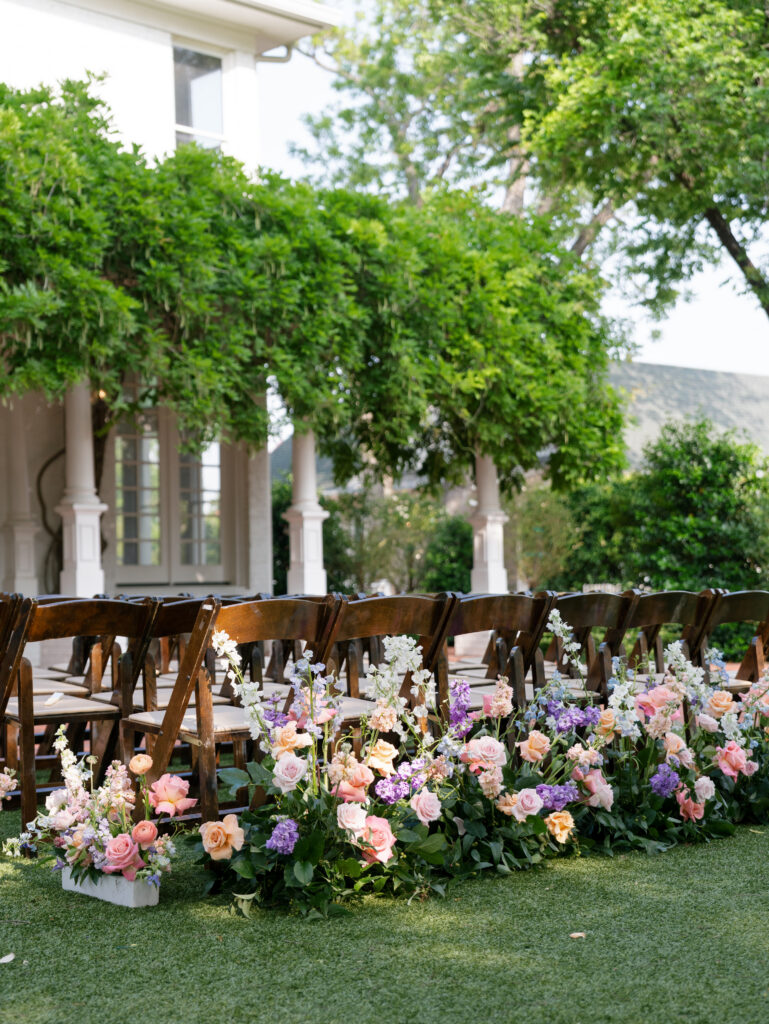 Outdoor wedding ceremony aisle lined with pastel flowers beside Woodbine Mansion.