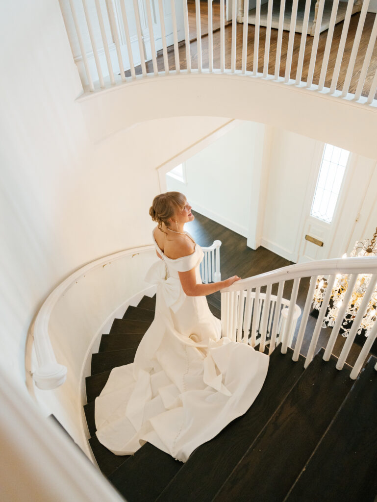 Bride walking down the curved staircase inside Woodbine Mansion before her wedding ceremony.