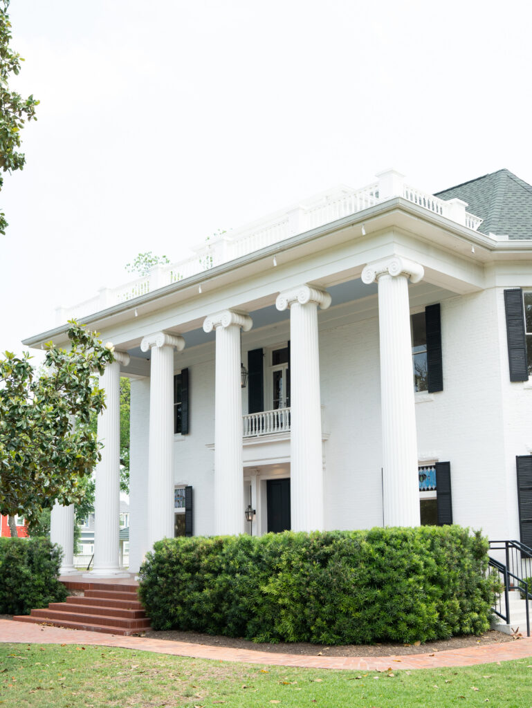 Historic white exterior and grand columns of Woodbine Mansion in Round Rock, Texas.