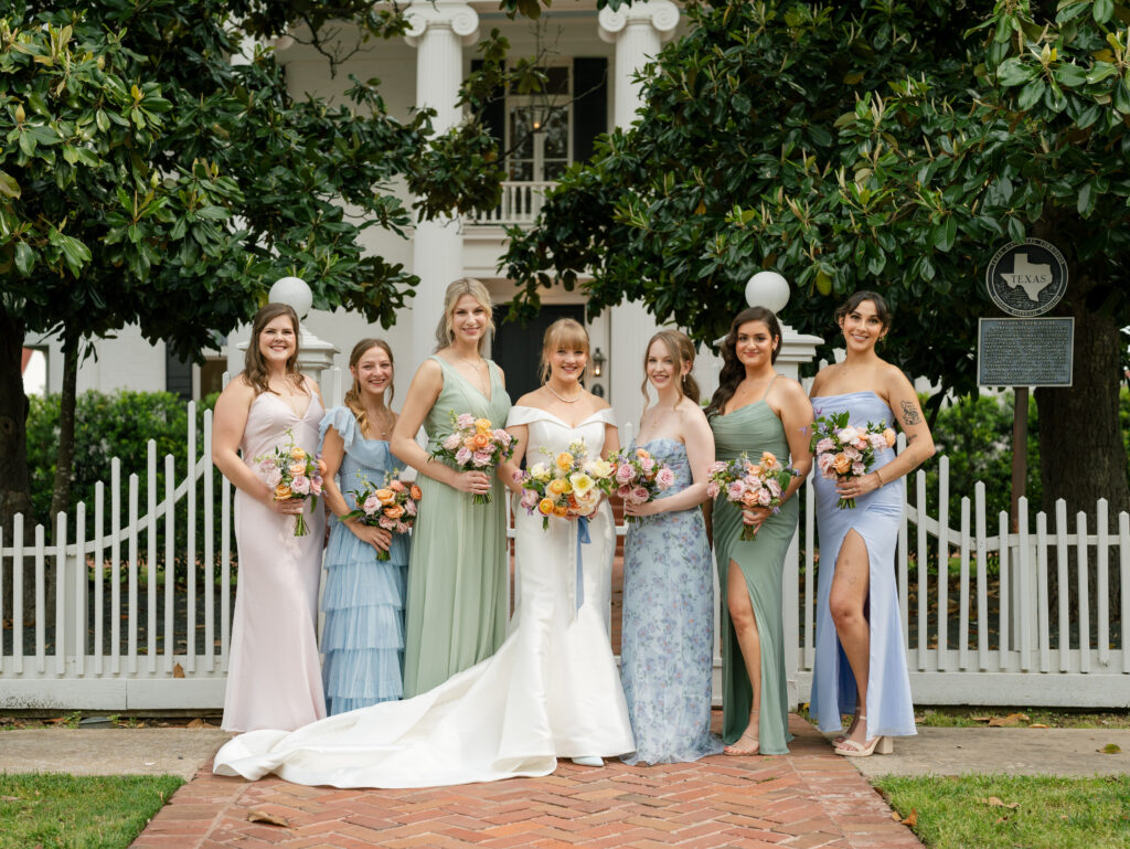 Bride and bridesmaids holding colorful bouquets outside Woodbine Mansion in Round Rock, Texas.